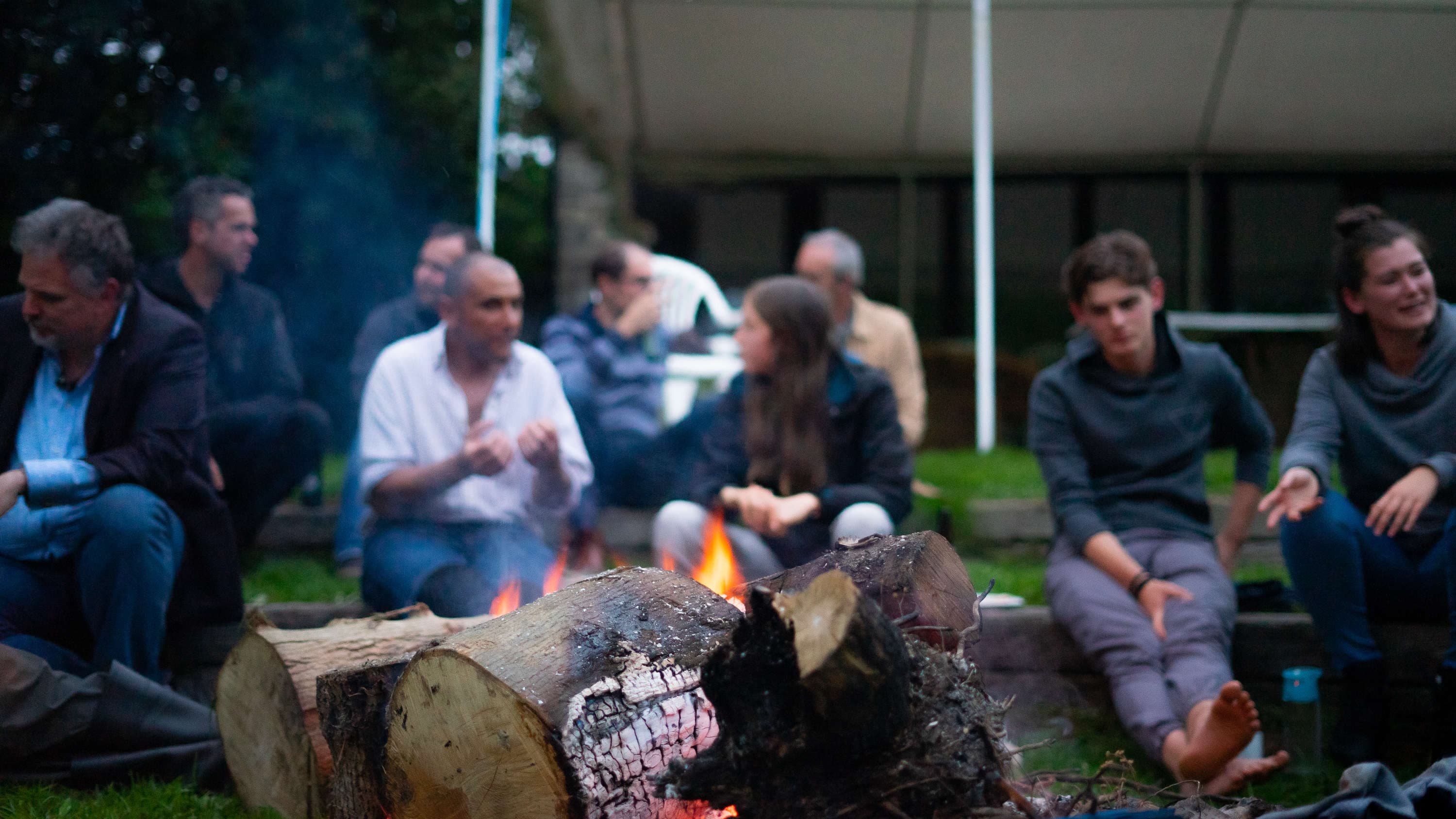 Friends gathered around a campfire by a lake at dusk